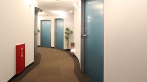 A hallway with blue doors, a red fire extinguisher, and a plant. - HOTEL LiVEMAX Korakuen (Tokyo)