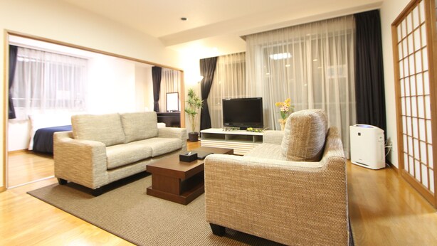 A modern living room with a sofa, coffee table, TV, and a large window with curtains. - HOTEL LiVEMAX Korakuen (Tokyo)