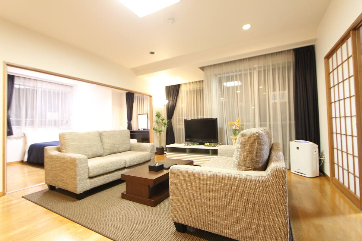 A modern living room with a sofa, coffee table, TV, and a large window with curtains.
