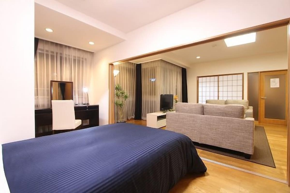 A hotel room with a bed, a desk, a chair, a sofa, and a television.