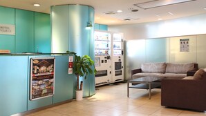 A reception area with teal walls, a reception desk, a vending machine, a potted plant, and a brown sofa. - HOTEL LiVEMAX Korakuen (Tokyo)
