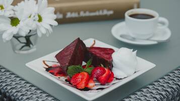 Ein Dessertteller mit Erdbeeren und einer weißen Nachspeise, eine Tasse Kaffee und ein Buch im Hintergrund.