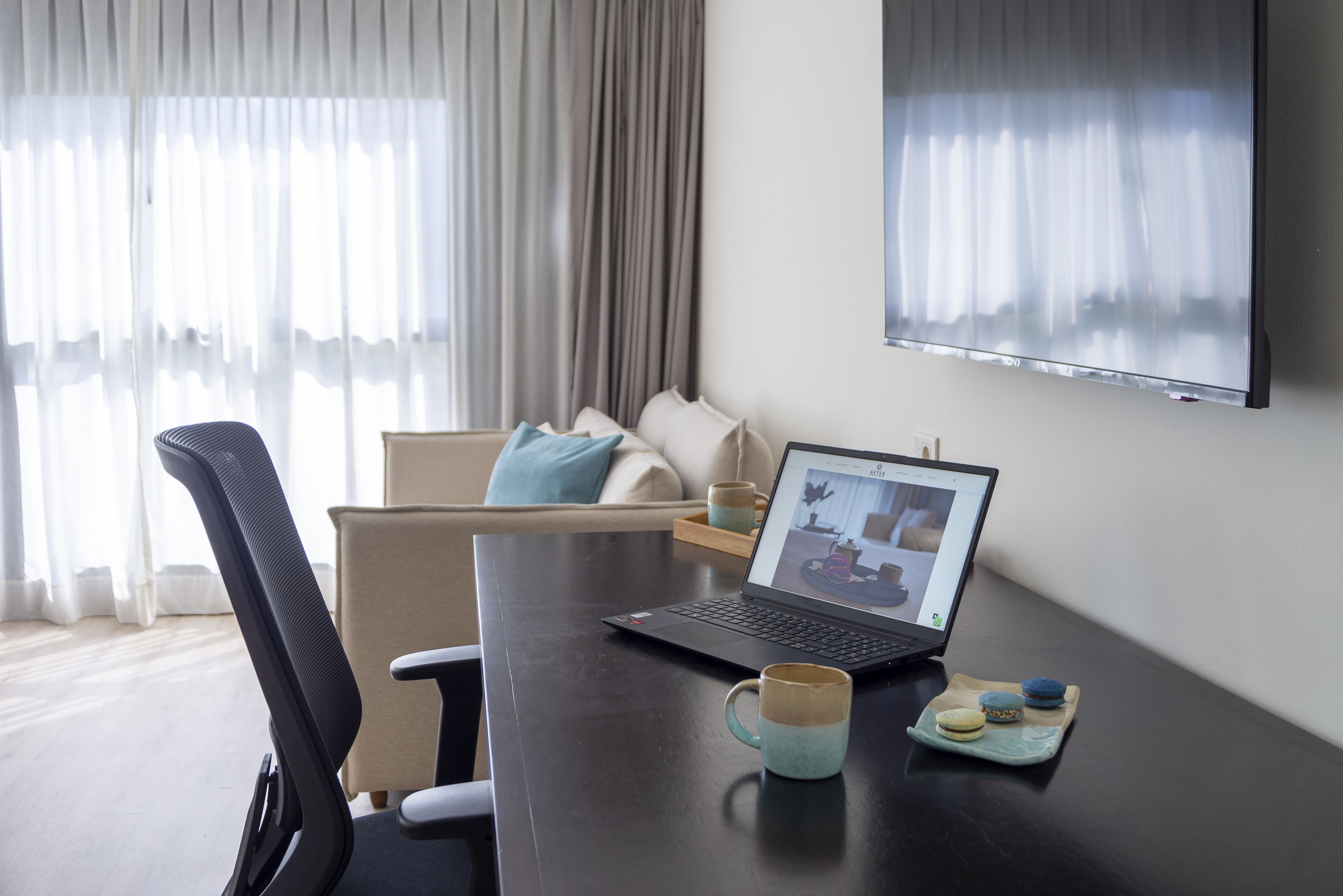 Una habitación de hotel moderna con una computadora portátil sobre una mesa, una taza de café y un plato con macarons.