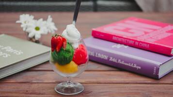 A dessert in a glass cup with a spoon, surrounded by books on a wooden table.