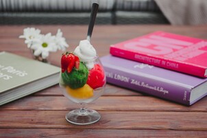 A dessert in a glass cup with a spoon, surrounded by books on a wooden table.