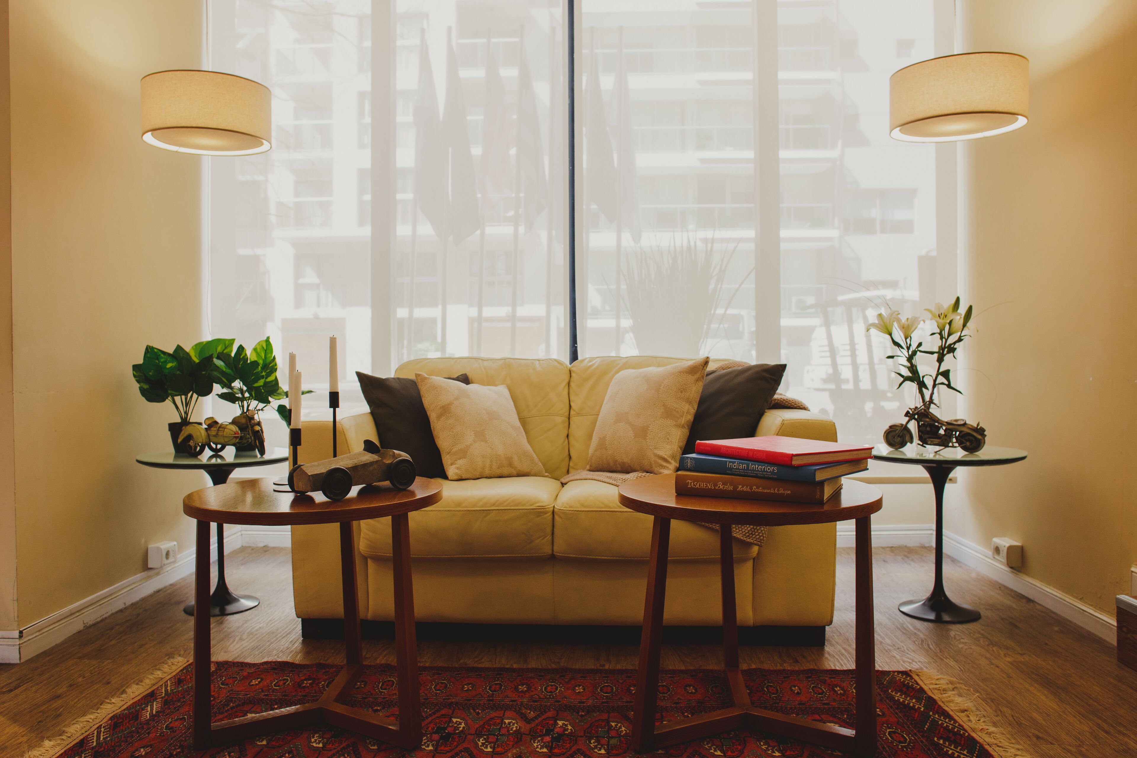 A living room with a sofa, two side tables, a potted plant, and a window with blinds.