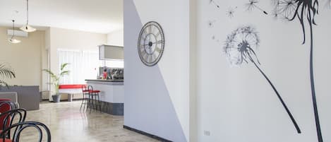 Un salón amplio con cocina, un comedor con sillas rojas y una pared con un reloj y una obra de arte de diente de león.