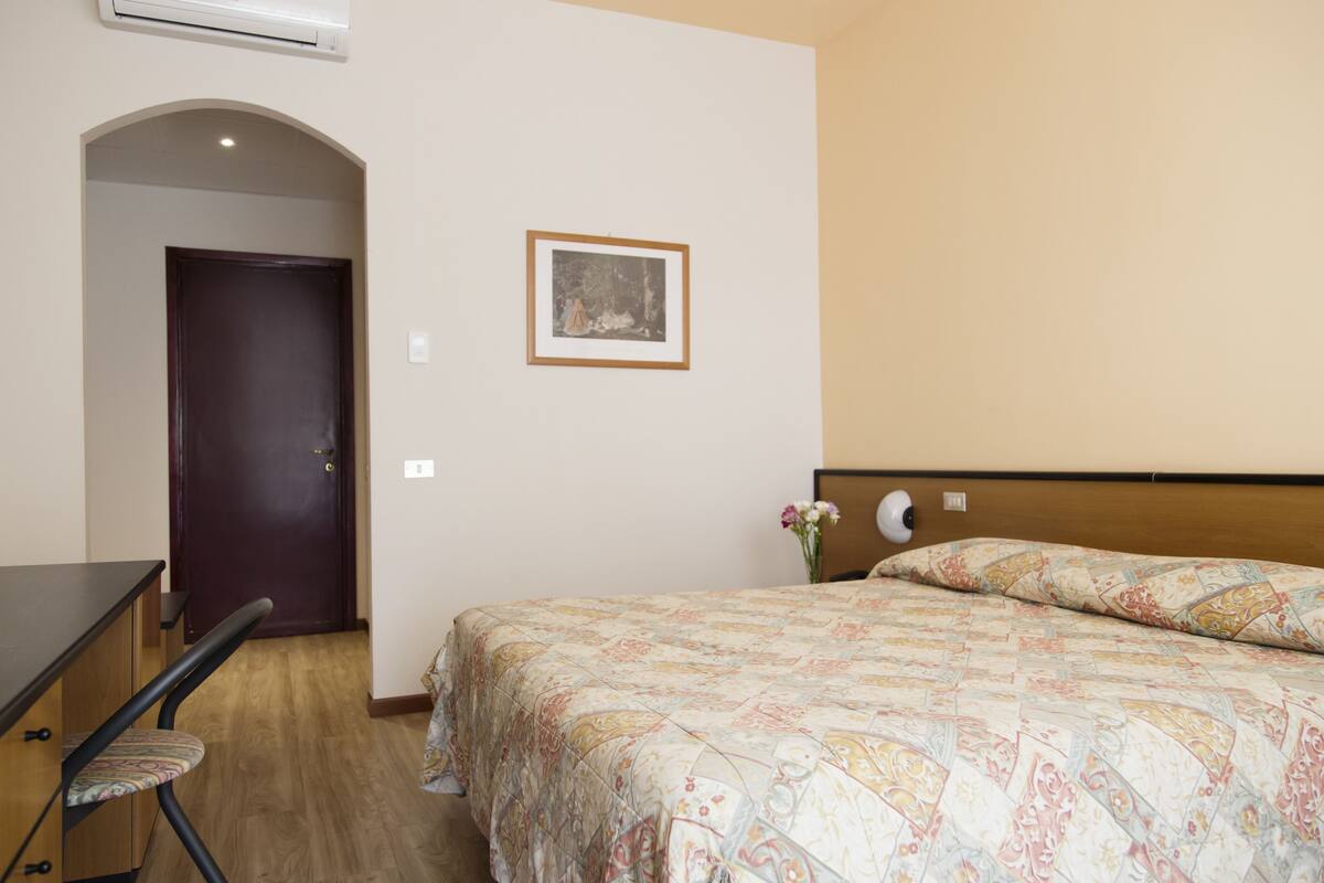 A hotel room with a bed, a desk, a chair, and a framed picture on the wall.