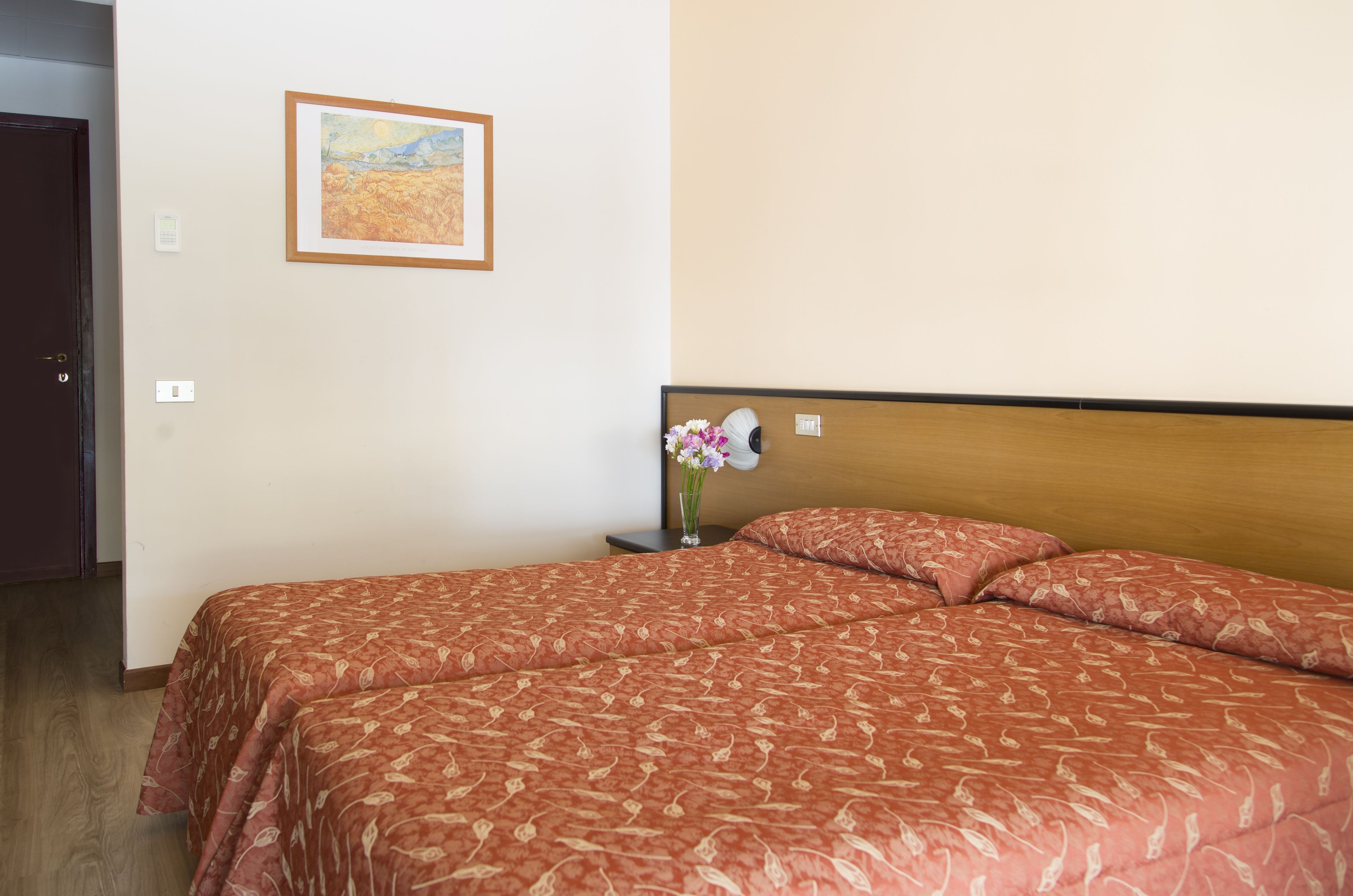 Een hotelkamer met een bed, een nachtkastje met een bloemetjesvaas en een schilderij aan de muur.