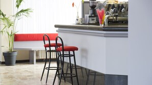 Una cocina con un banco rojo, dos taburetes, una cafetera y una planta en maceta.