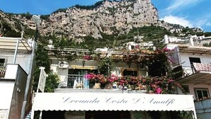 Un edificio con un letrero que dice "Locanda Costa D'Amalfi" y una montaña al fondo.