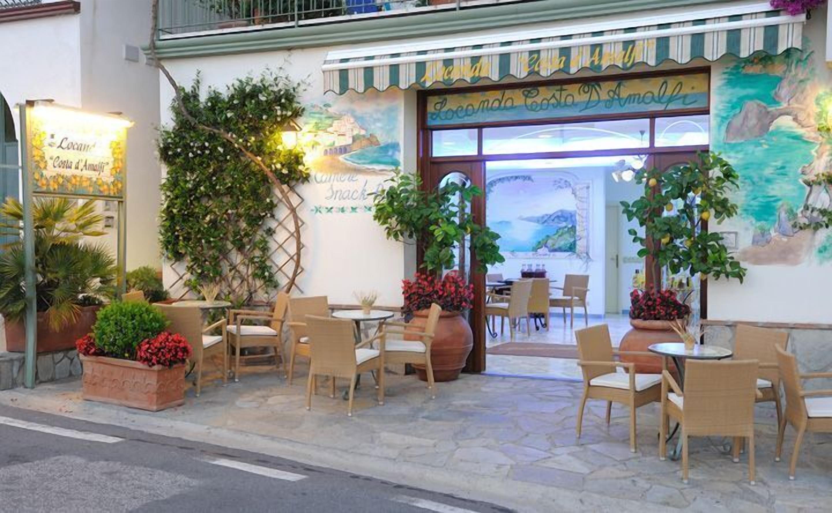 A restaurant with outdoor seating, a mural of a coastal scene, and potted plants.