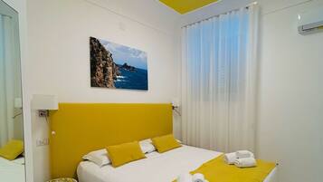 A hotel room with a bed, a small table, a painting, and a window with curtains.