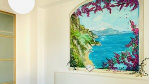 Habitación de hotel con cama, almohadas amarillas, toallas blancas, un cuadro de una escena costera y una lámpara colgante.
