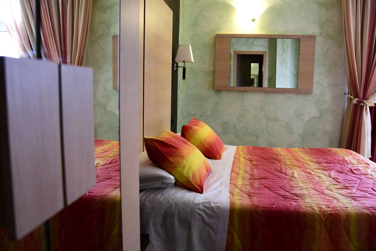 Habitació d'hotel amb dos llits, un mirall, una tauleta de nit i una làmpada.