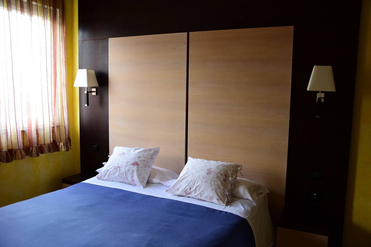 Habitació d'hotel amb un llit gran, dues làmpades de nit i una finestra amb cortines.