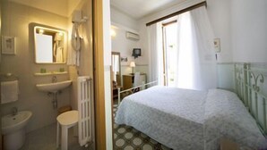 Un dormitorio con cama, ventana con cortinas, radiador y baño con lavabo y espejo.