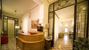 Un hall de hotel con piso a cuadros, una recepción y un espejo grande con paneles de vidrio decorativos.