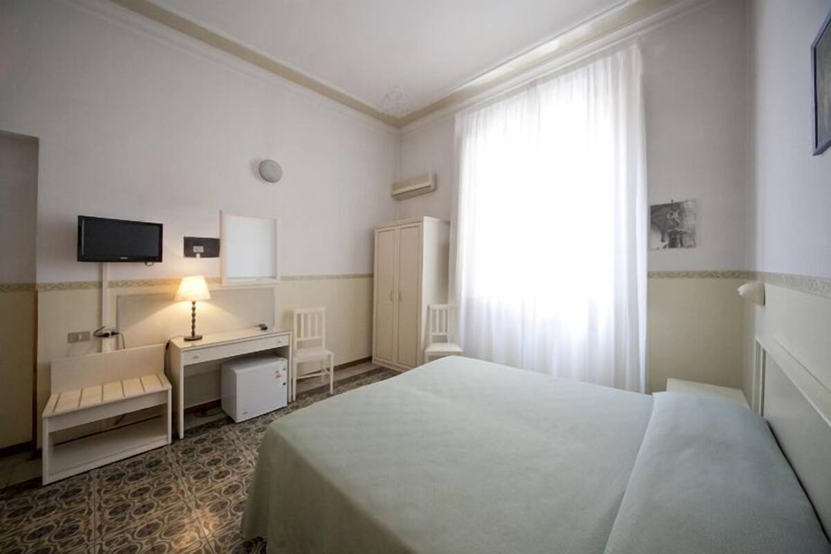 A hotel room with a bed, a desk, a chair, a television, and a wardrobe.