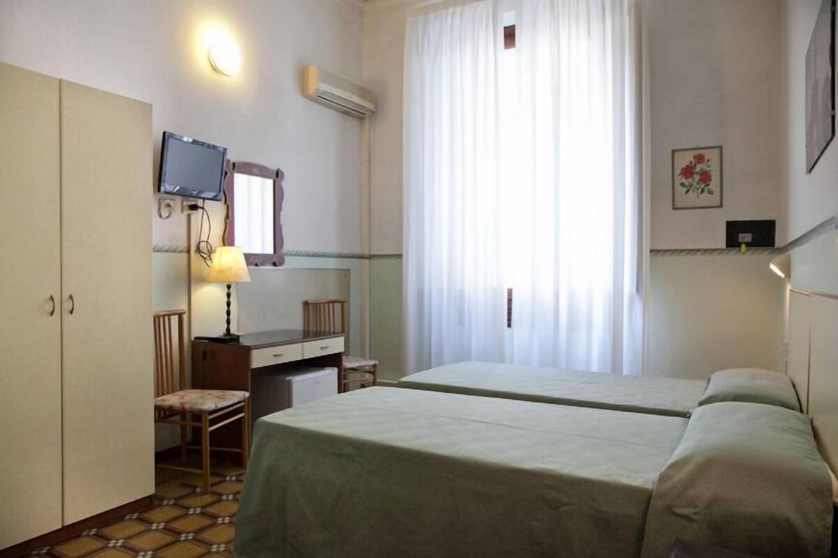 A hotel room with two beds, a desk with a chair, a television, and a window with curtains.
