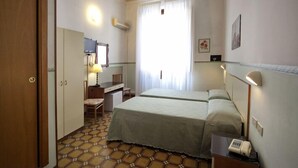 Habitación de hotel con cama, escritorio, silla, teléfono y ventana con cortinas.