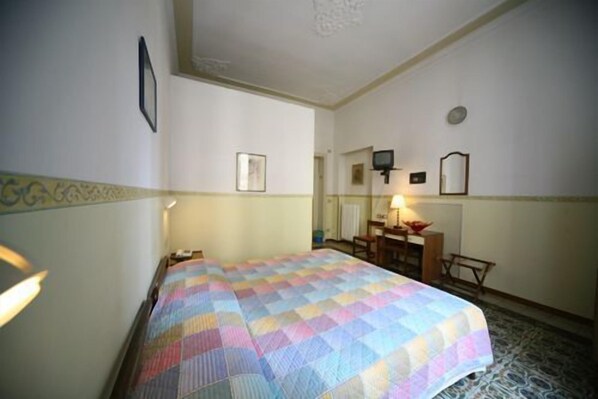 A hotel room with a bed, a desk, a chair, a television, and a mirror.
