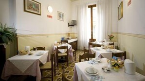 Un comedor con mesas dispuestas para cuatro, sillas y un amplio ventanal con cortinas.
