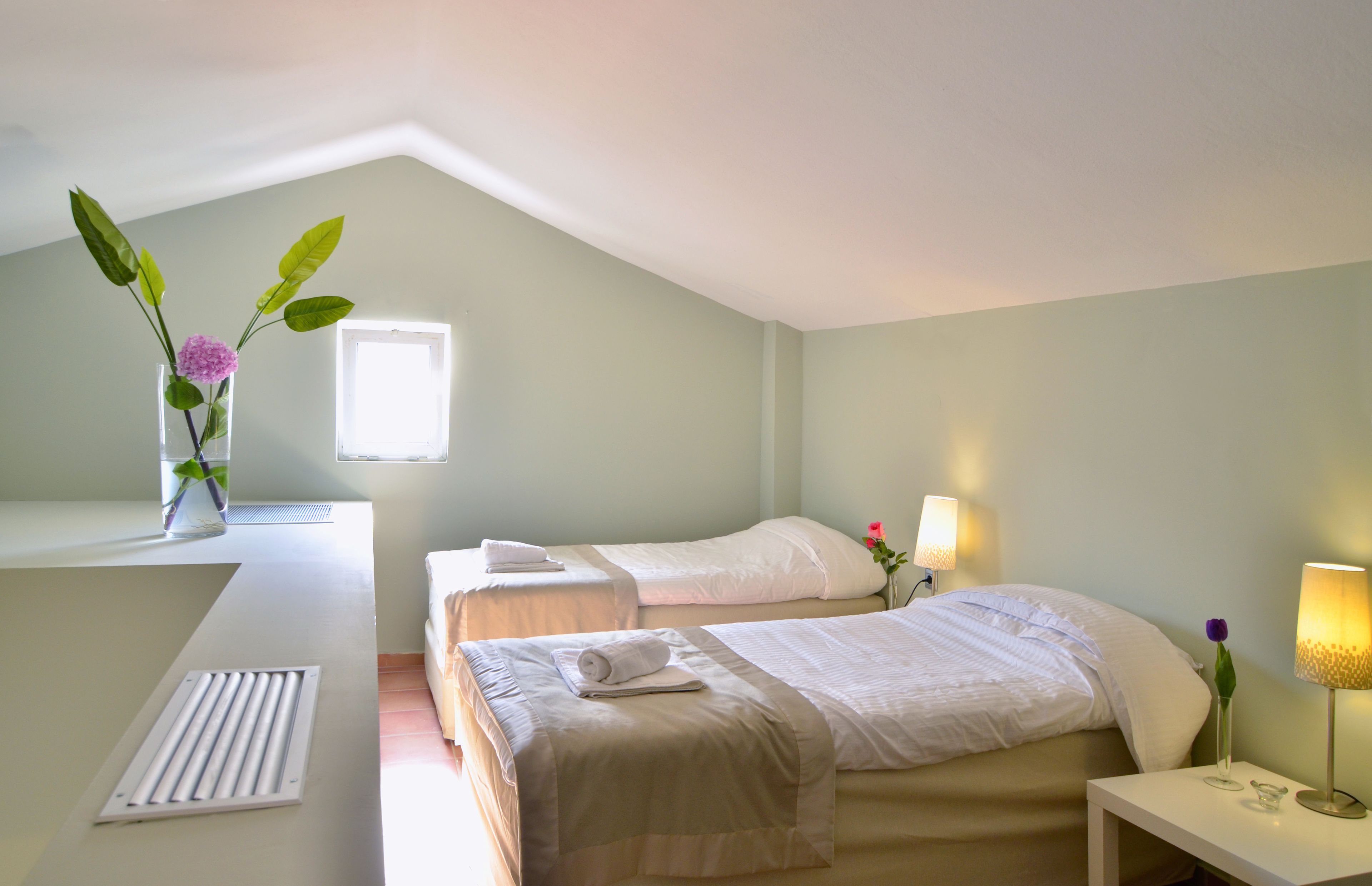 A hotel room with two beds, a window, a desk, and a radiator.