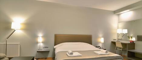 Una habitación de hotel con cama, mesitas de noche, escritorio, silla y espejo.