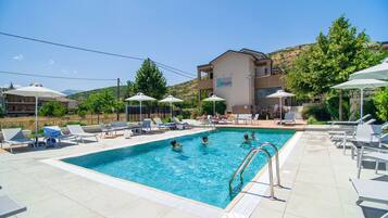 A swimming pool with lounge chairs and umbrellas, surrounded by buildings and trees.