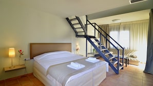 A hotel room with a bed, a nightstand with a lamp, a flower, a staircase, and a seating area with a sofa and curtains. - Ellopia Point Hotel (Ioannina)