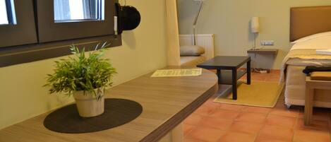 Habitación de hotel con cama, mesita de noche, lámpara y planta en maceta sobre un mostrador de madera.