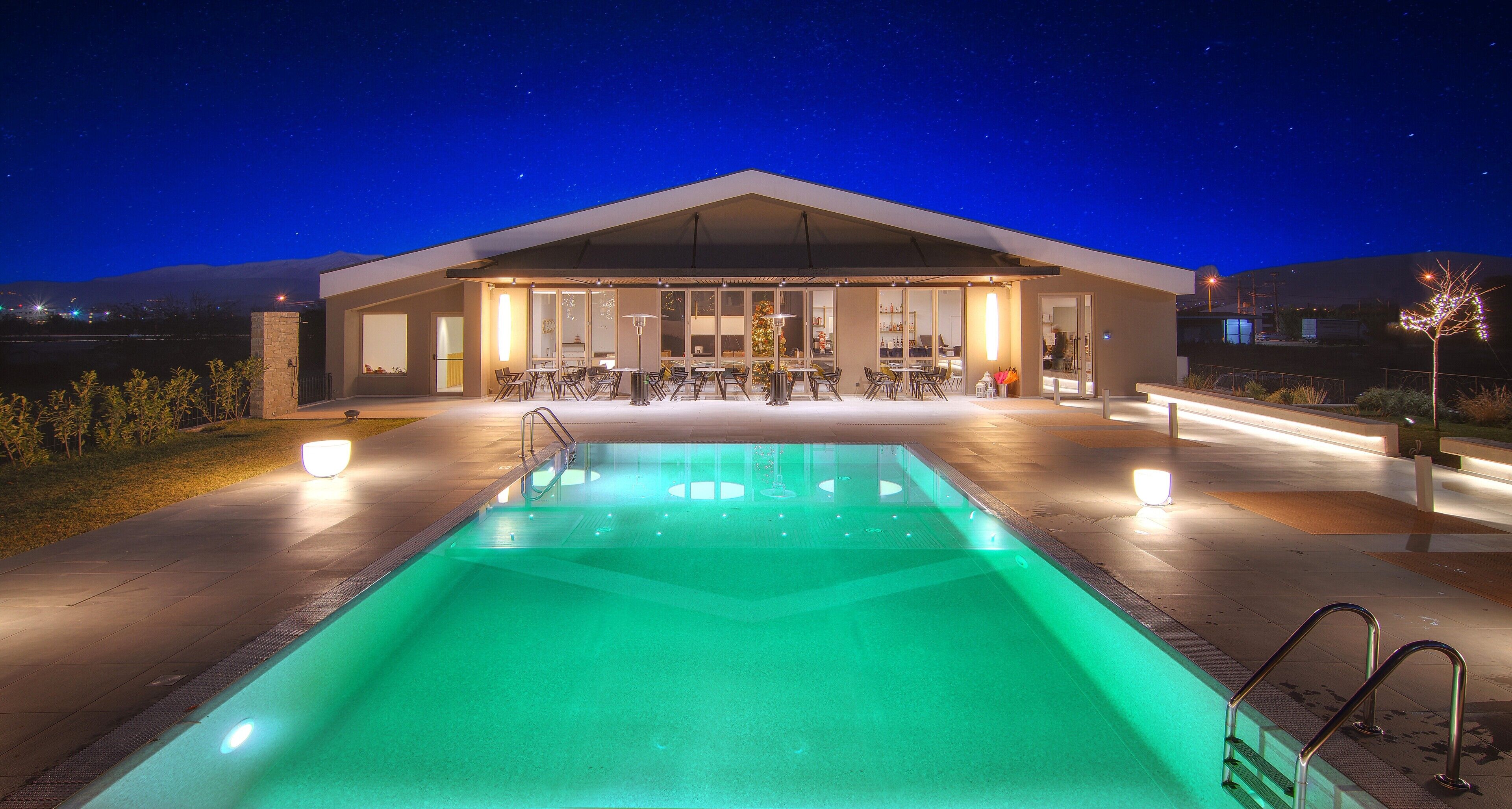 A modern building with a swimming pool, outdoor seating, and a covered patio area.