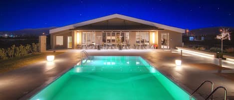 Un edificio moderno con piscina, mobiliario exterior y un patio cubierto.