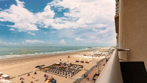 Vista a la playa desde un balcón, con arena, sombrillas y una torre de salvavidas.