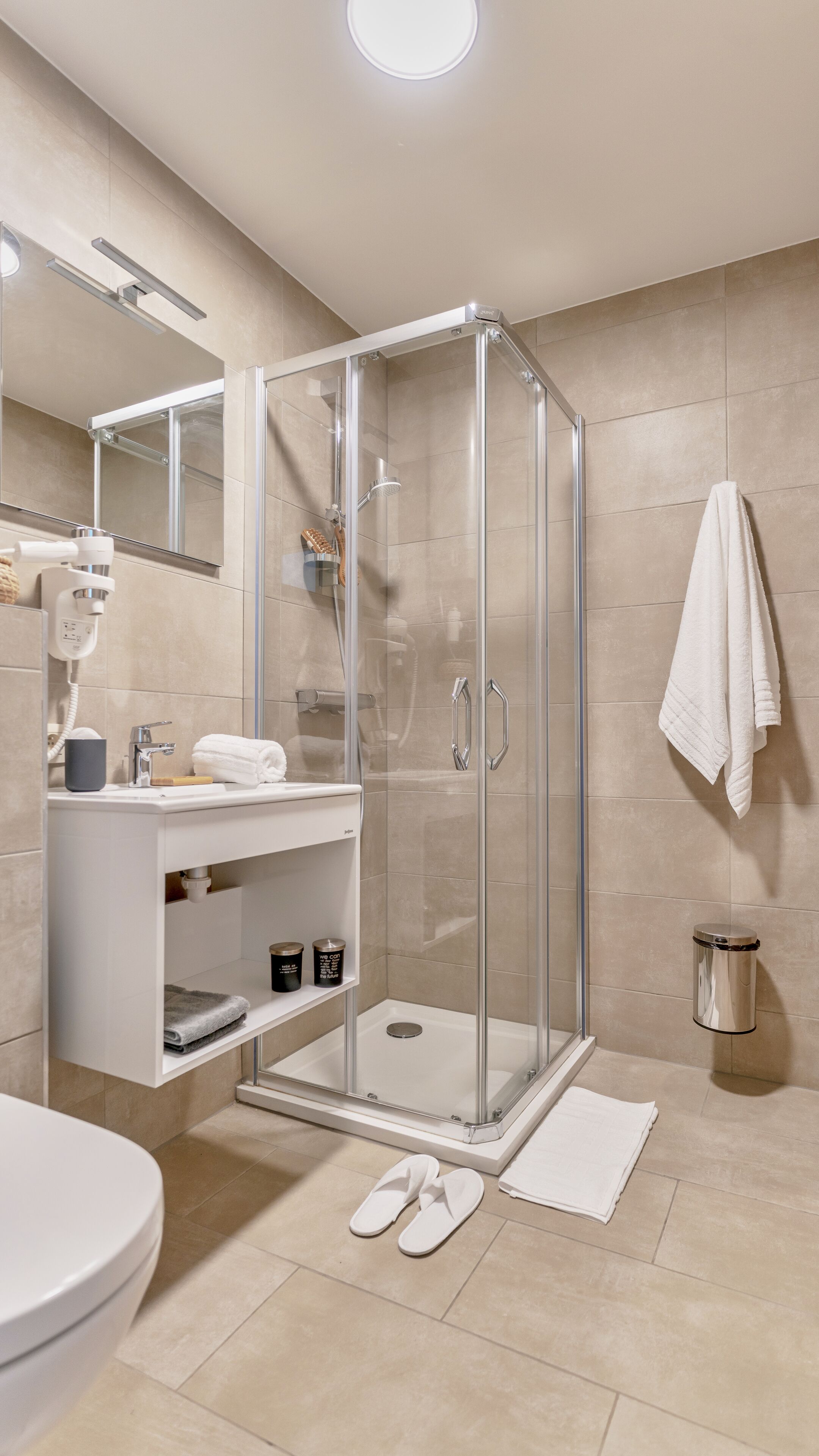 Et moderne badeværelse med en glasafskærmet brusekabine, en hvid vask og et toilet.
