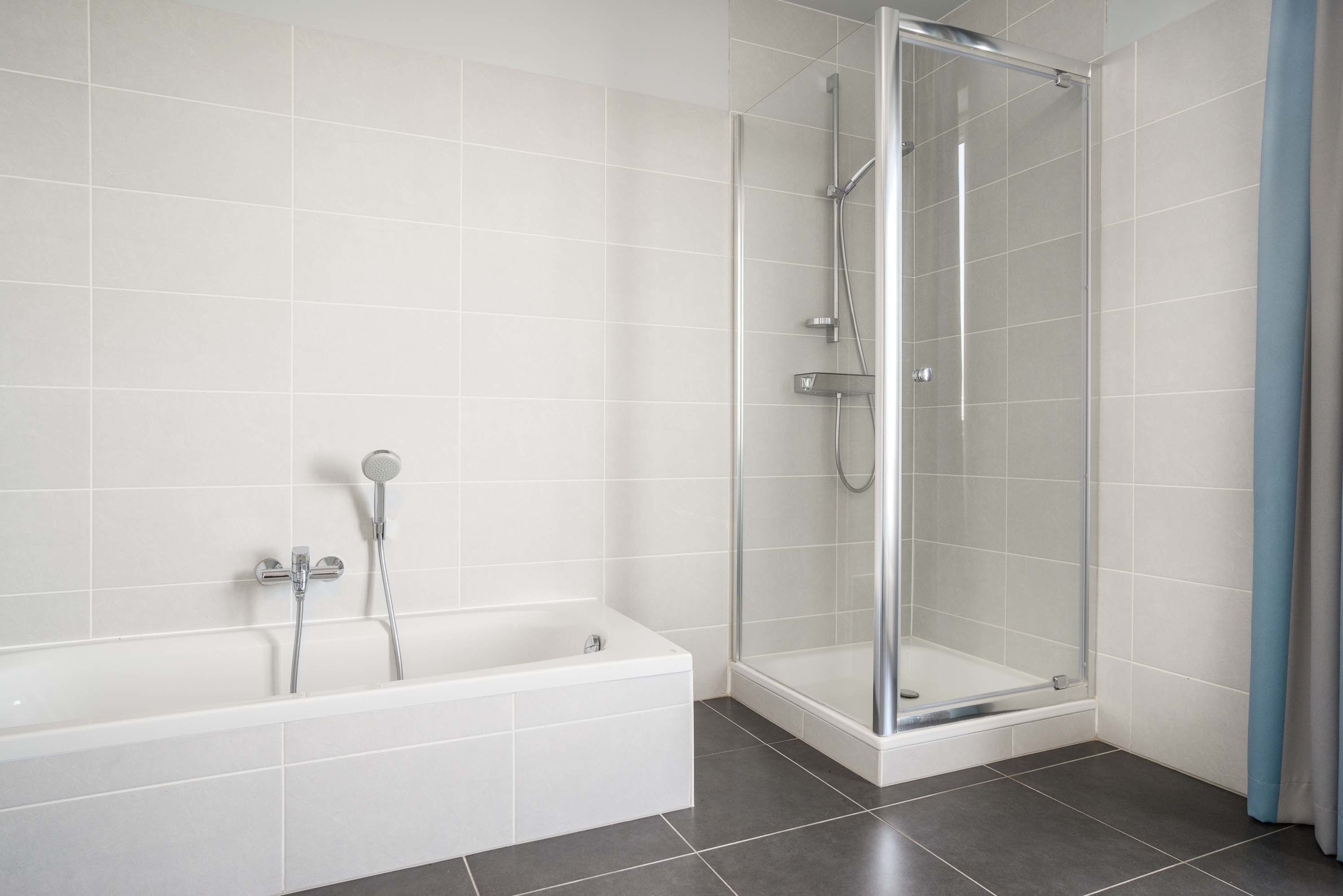 Une salle de bain équipée d’une baignoire, d’une douche et d’un espace de douche séparé par des parois en verre.
