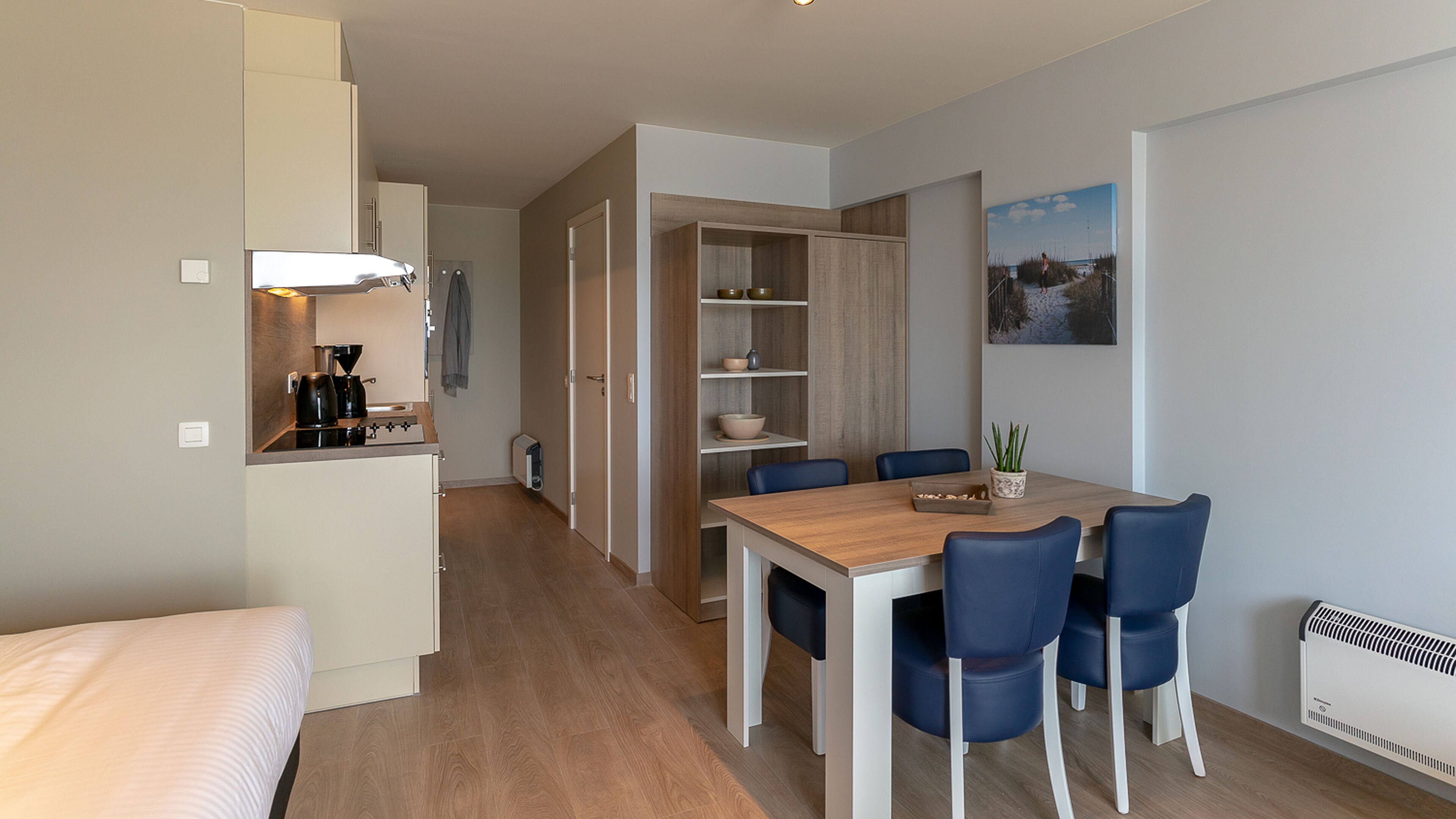 Een kleine hotelkamer met kitchenette, een eethoek met blauwe stoelen en een bed.
