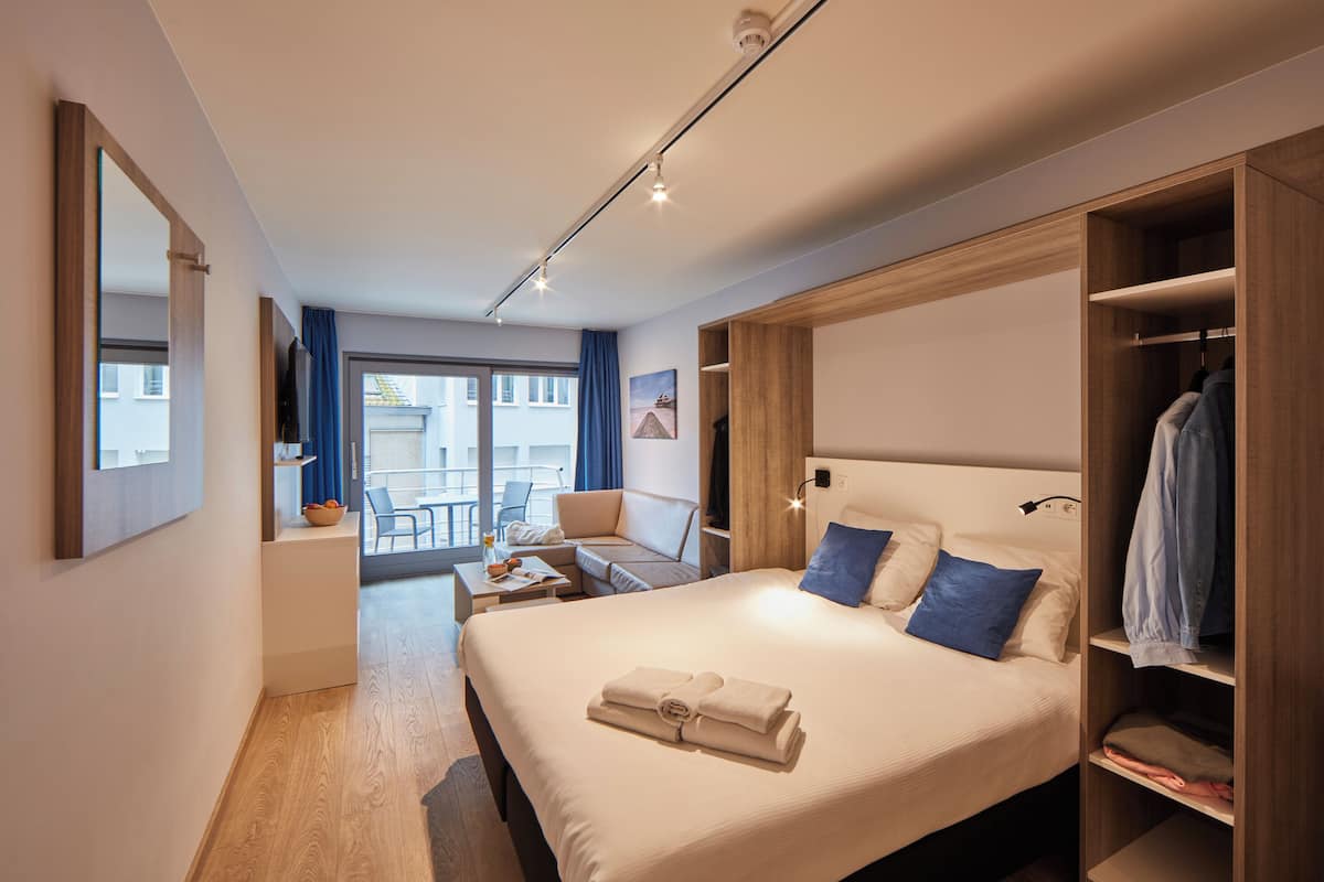 Una habitación de hotel moderna con una cama grande, una zona de estar con una mesa y vistas al exterior.