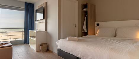 Habitación de hotel moderna con una cama grande, un armario, un televisor y vistas a la playa.