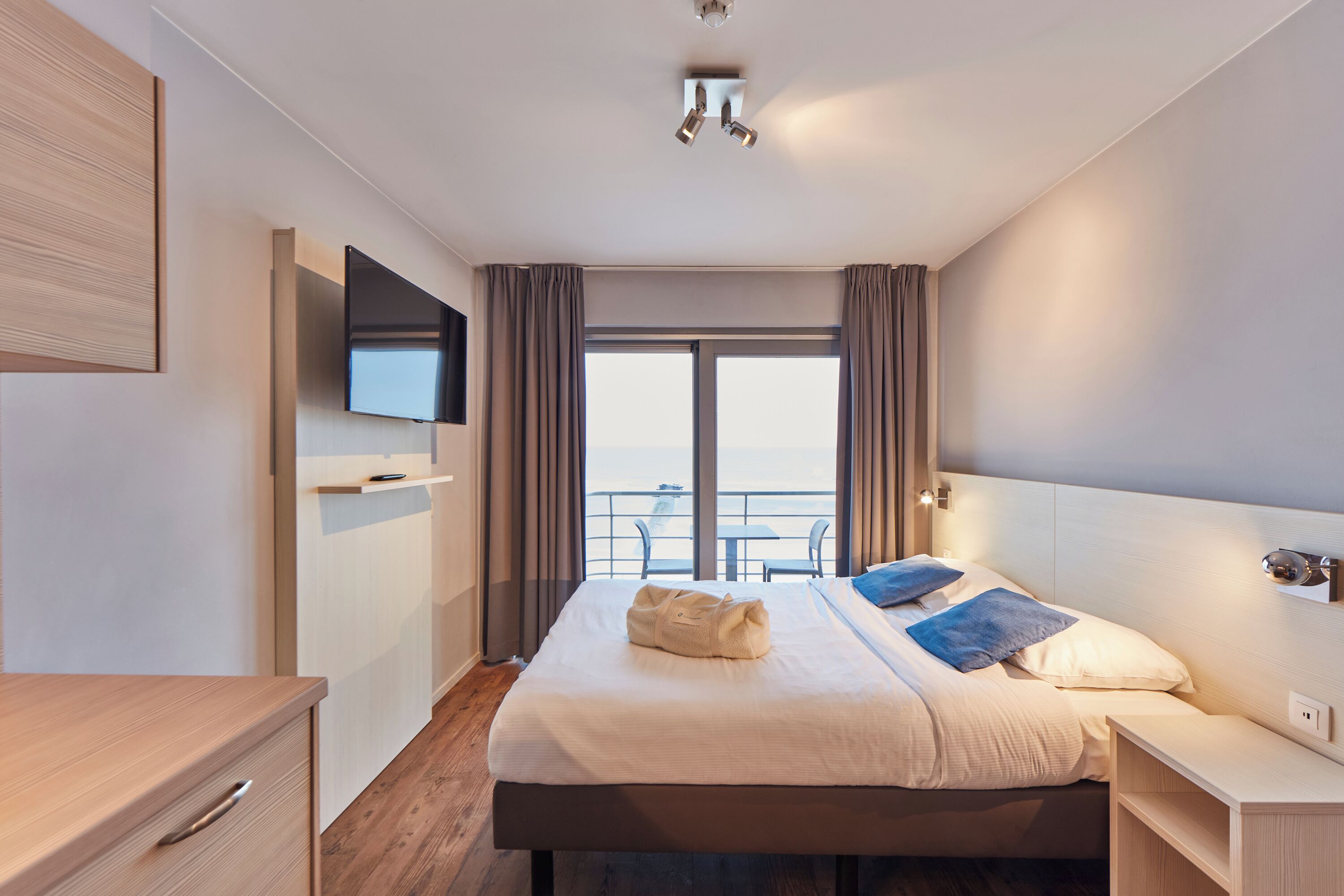 Habitación de hotel con cama, mesita de noche, televisor y vista al balcón.