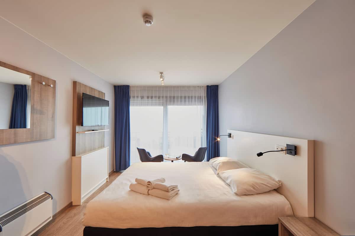 Una habitación de hotel moderna con una cama grande, una mesita de noche, una silla, un escritorio y vistas a la ciudad a través de la ventana.