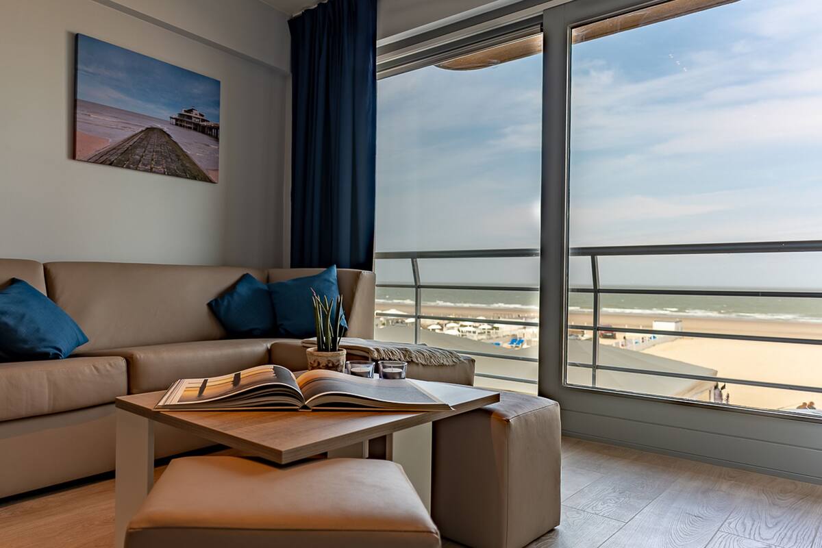 Una sala de estar moderna con un sofá color beige, una mesa de centro y vistas a la playa a través de grandes ventanales.