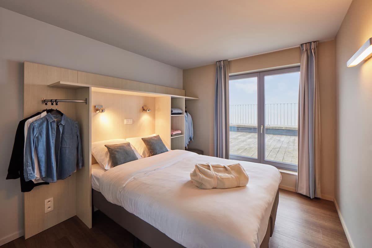 Habitación de hotel con cama, armario, ventana con cortinas y vistas al exterior.