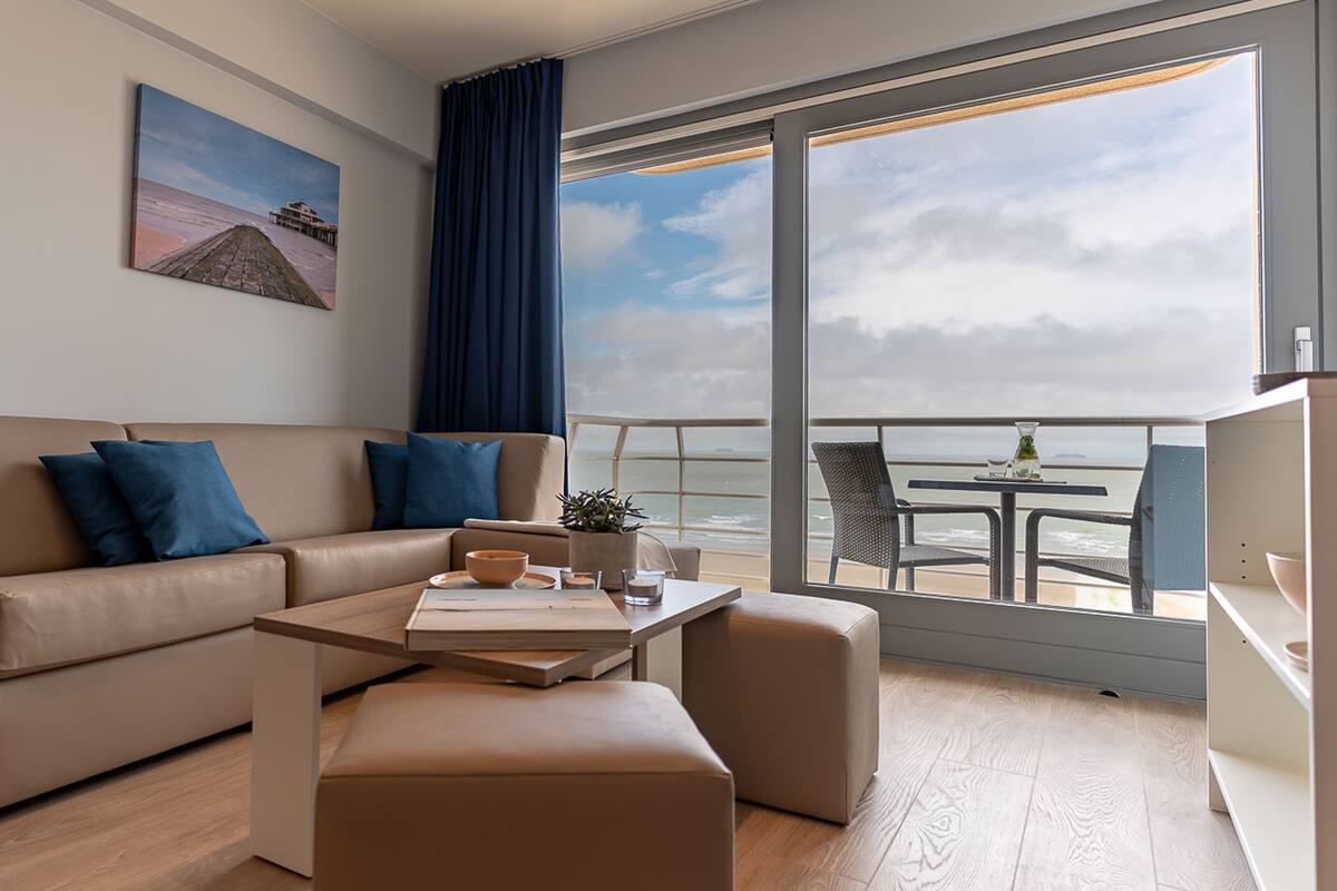Un salón moderno con sofá, mesa de centro y vistas al océano a través de amplios ventanales.