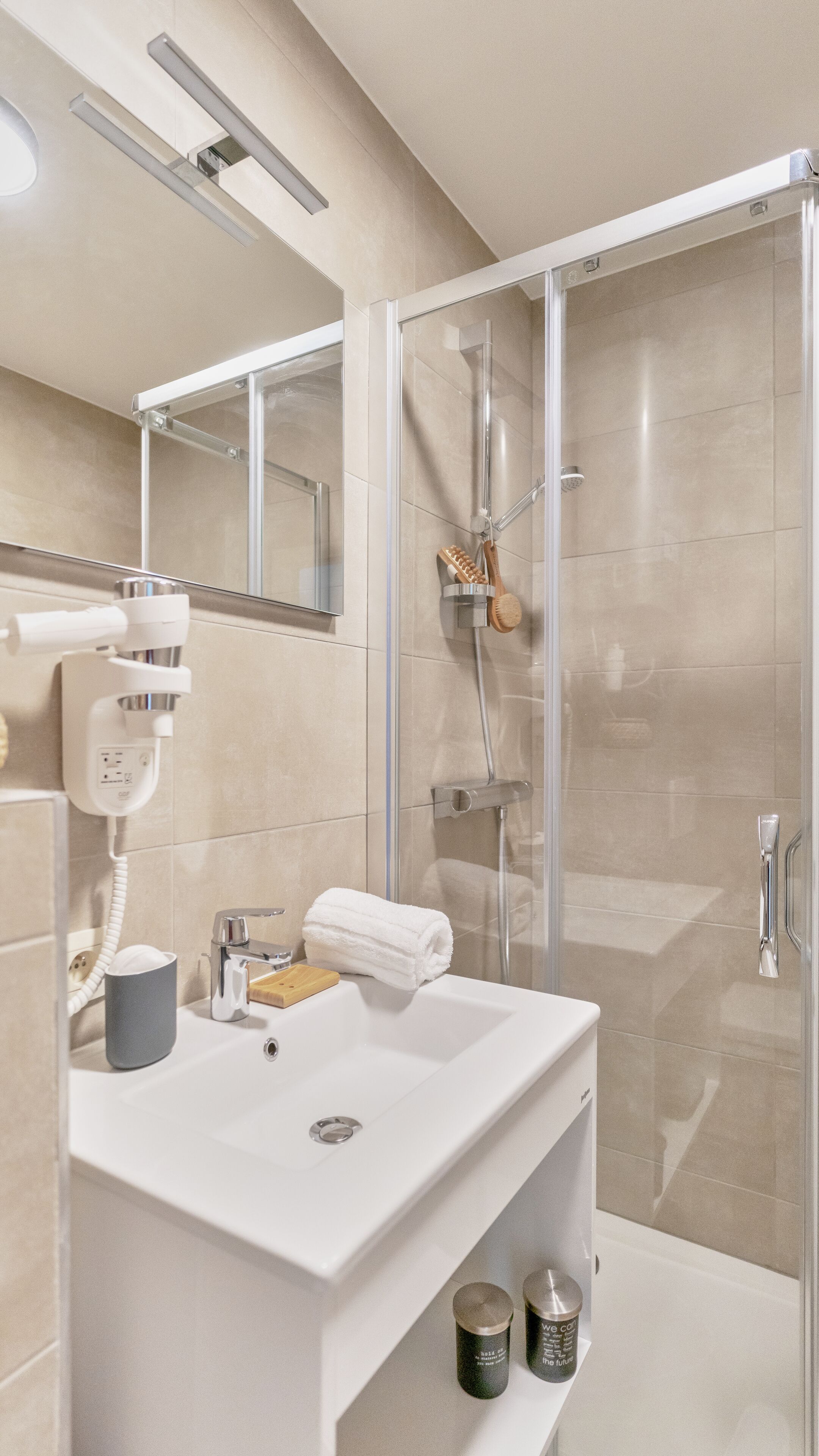 A modern bathroom with a glass shower enclosure, a white sink with a mirror above it, and a hairdryer on the wall.