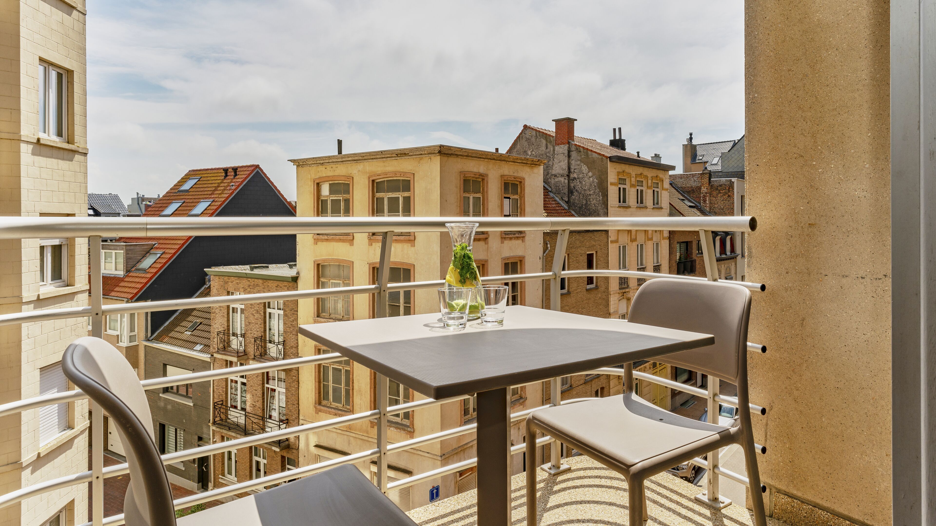 A balcony with a table and chairs, overlooking a cityscape with historic buildings.