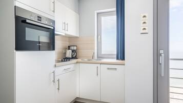 A compact kitchen with white cabinets, a Bosch oven, a coffee maker, and a window with blue curtains.