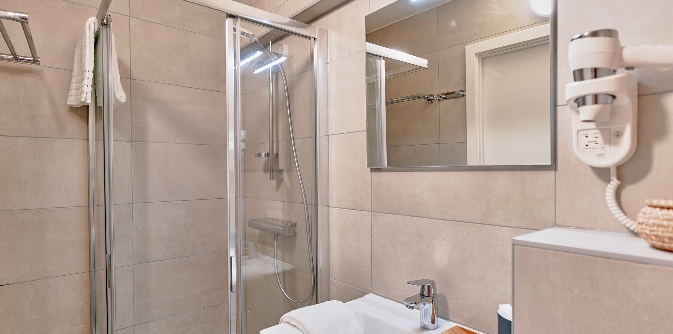 A modern bathroom with a glass-enclosed shower, a white sink, and a hairdryer mounted on the wall.