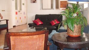 A living room with a black sofa, red cushions, a wicker chair, a round table, and a potted plant. - Puerta del Sol Rooms (Madrid)